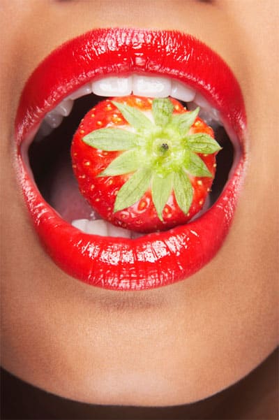 Girl eating straberry showing white teeth and red lips