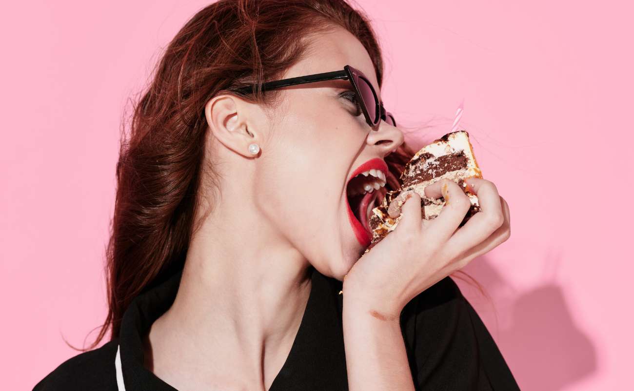 woman eating enjoying cake in pink background