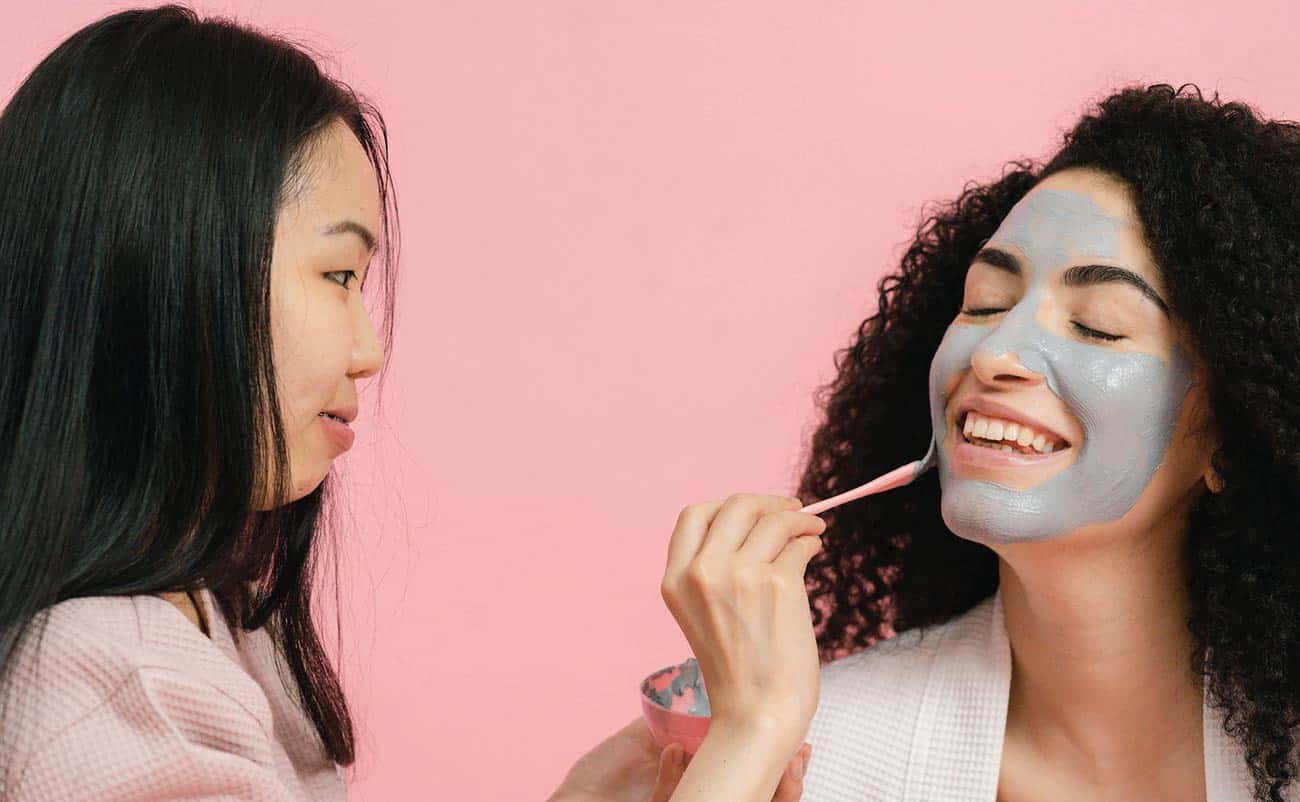 women applying skin care product on face at salon