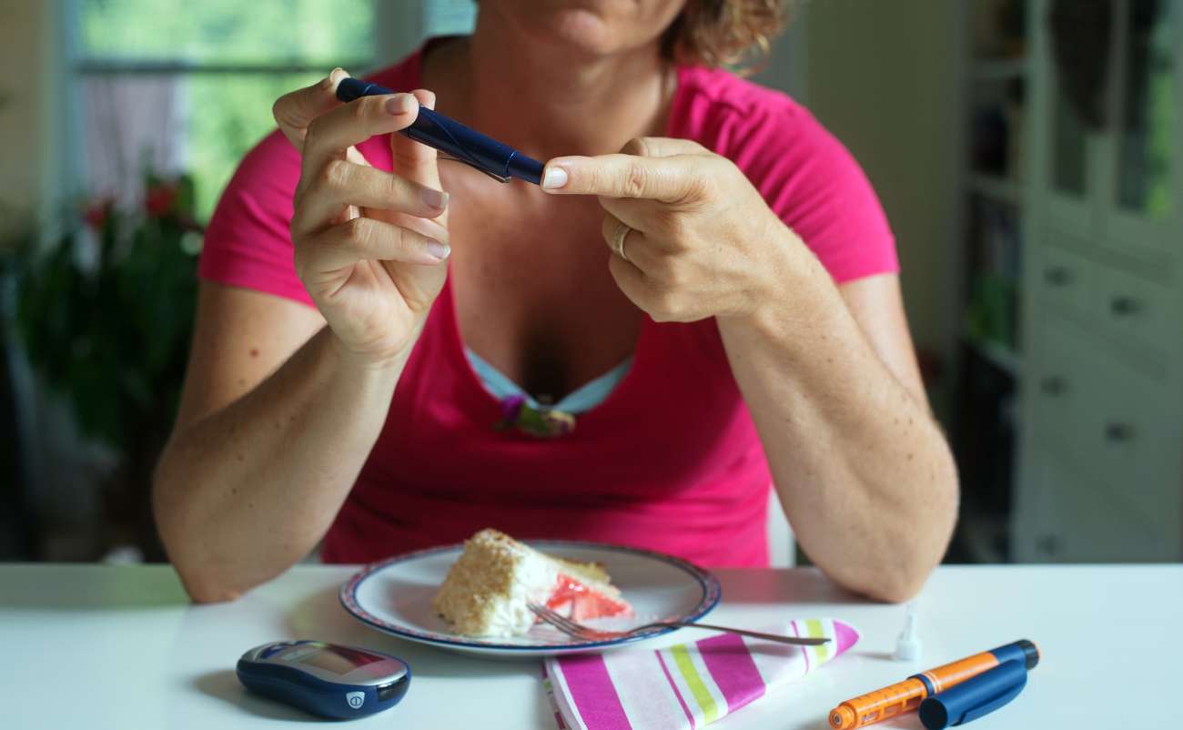 women checking blood sugar at home while eating cake