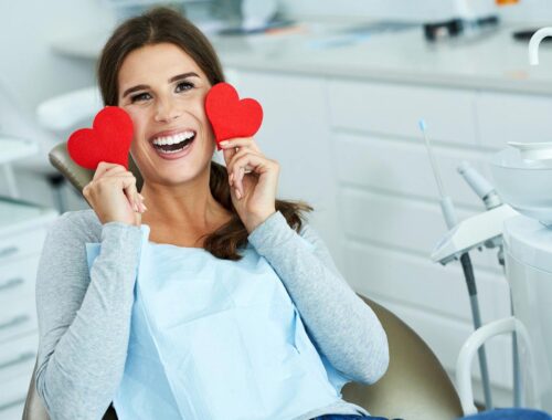 Women smilling and showing her white teeth with two red heart in hand