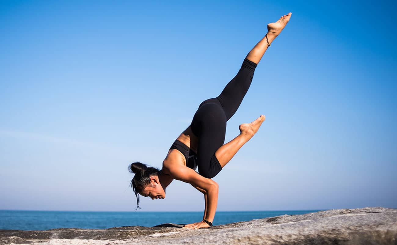 women doing gymnastics on rock beside blue ocean in black costume