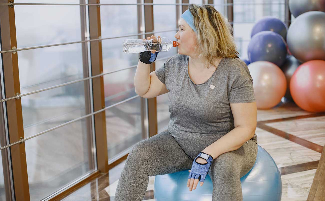 women drinking water sitting on ball at gym